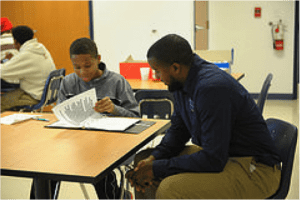A young boy works on homework with the assistance of a tutor from the JCPS program.